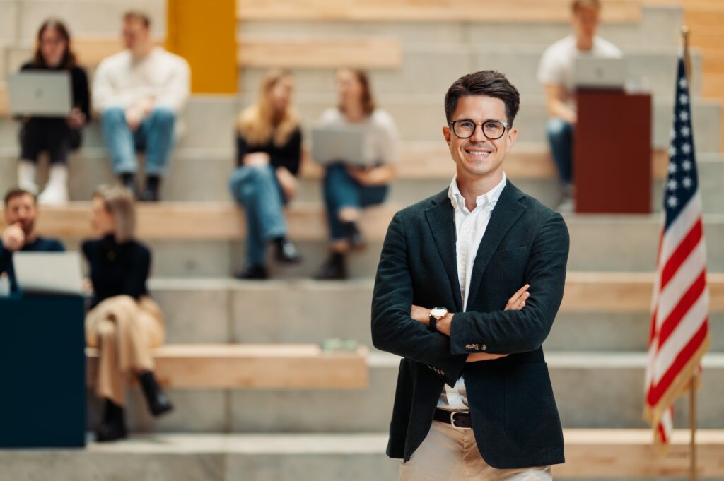 Jonas von Epro 360 steht vor einer Gruppe Studierender in einem modernen Hörsaal mit US-Flagge im Hintergrund.
