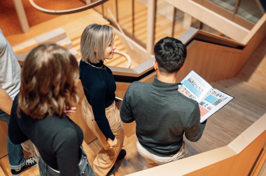 Gruppe von Studierenden geht eine Treppe hinunter, während Jonas von Epro 360 eine Broschüre hält.
