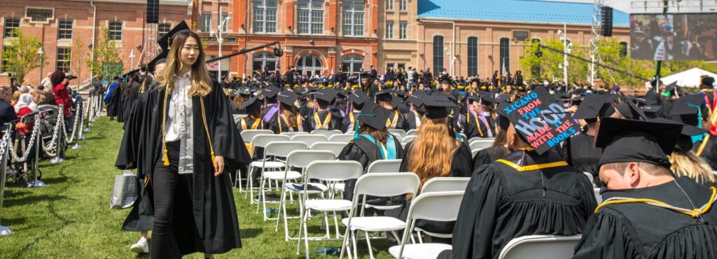 Graduation ceremony outside a building with graduates seated in caps and gowns.